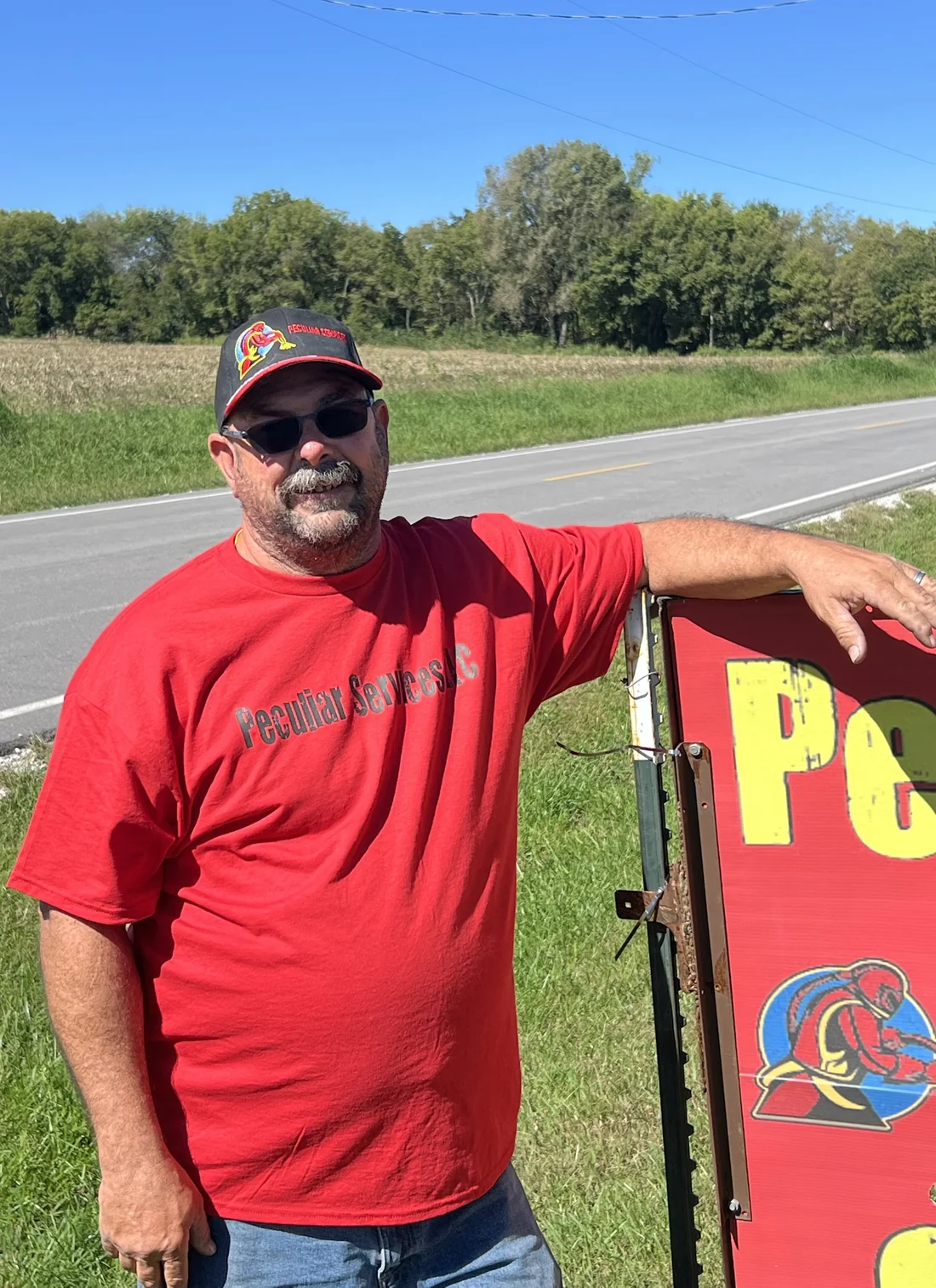 Carl Glowczewski beside the Peculiar Services sign on State Route D